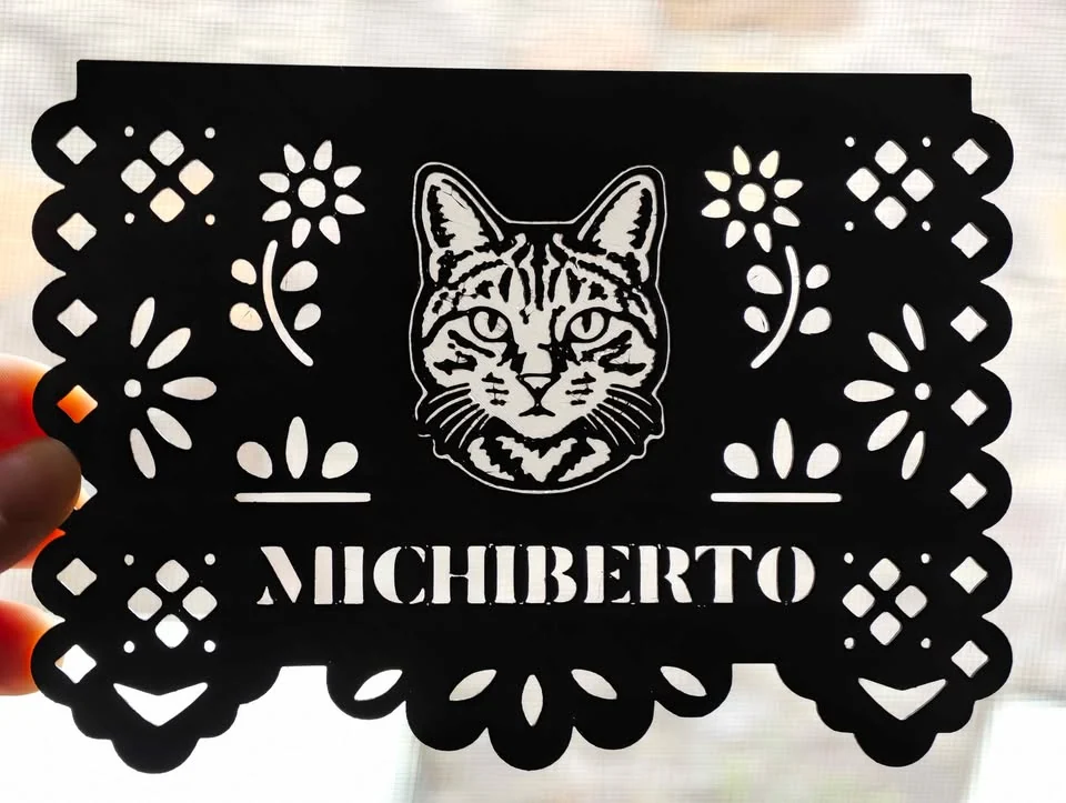 The finished 3D-printed papel picado: a black sheet with a cat portrait and the name Michiberto